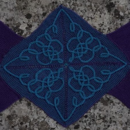 A knitted square with a purple background. Green cables swirl across the square in a repeating celtic knot pattern.