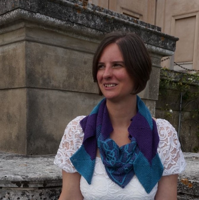 Front view of woman sitting against a pillar wearing a purple and green wrap around her neck.