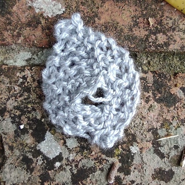 a handknit beech leaf lays on an old brick wall