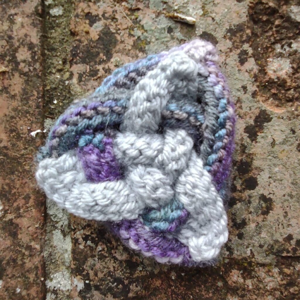 a handmade celtic knot in purple and silver sits on an old brick wall