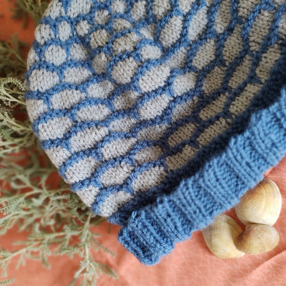 a close up photo of a blue and grey beanie hat, showing the ridged colour work details.