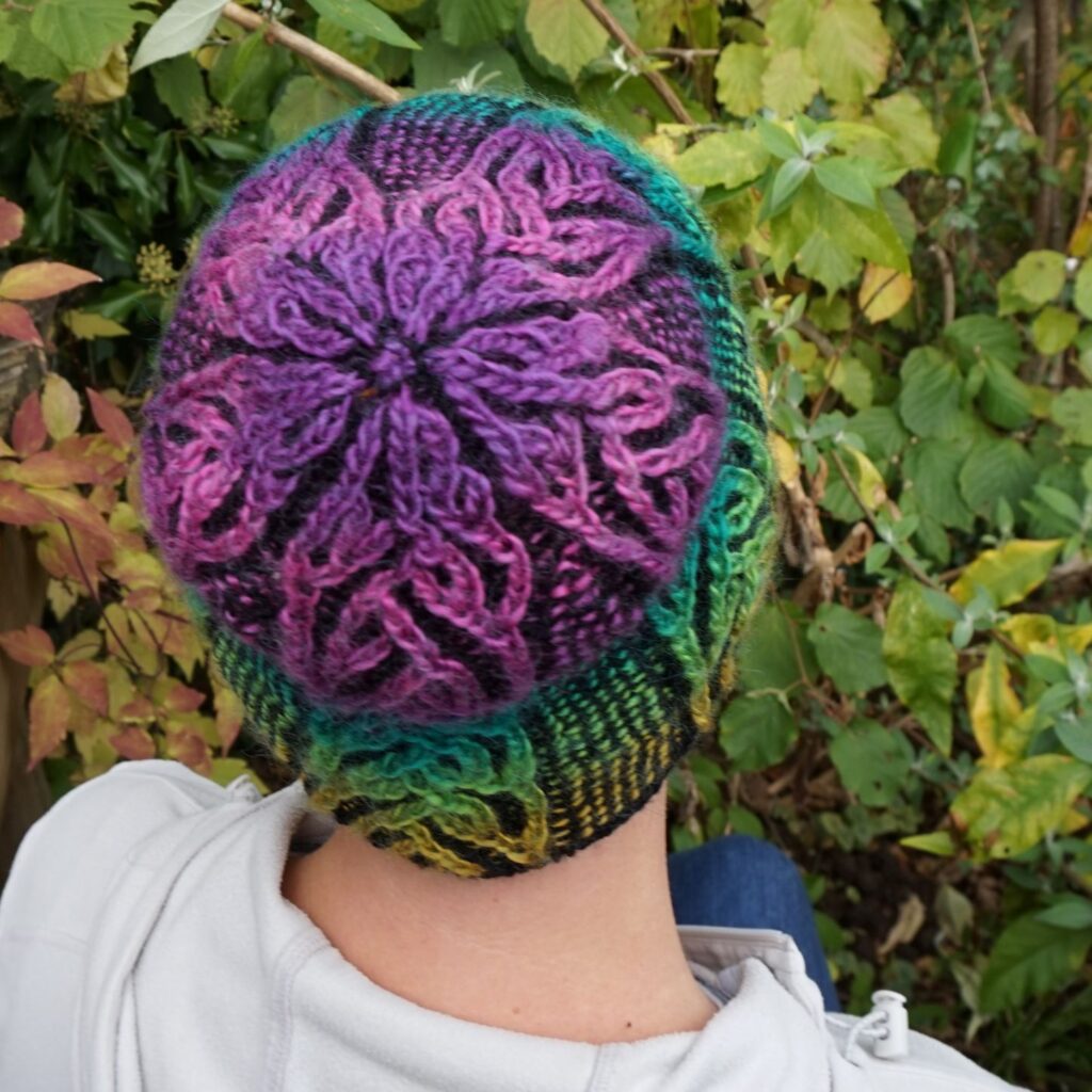 the camera looks down on the back of a hat. the crown is visible, with purple cables decreasing to a point.
