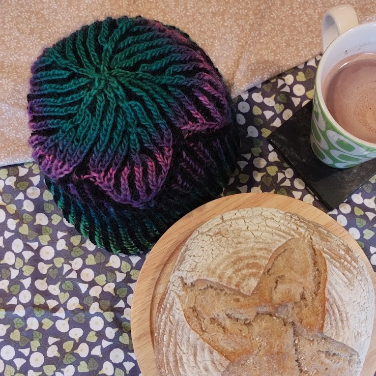 the camera looks down on a hat sitting next to a loaf of bread and a mug of tea. The hat and bread have a similar star design on the top.