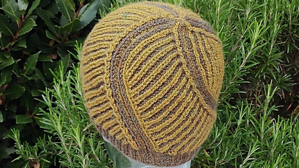 The crown of a yellow brioche hat is towards the camera. Stripes of brown twirl round the hat, coming together at the crown.