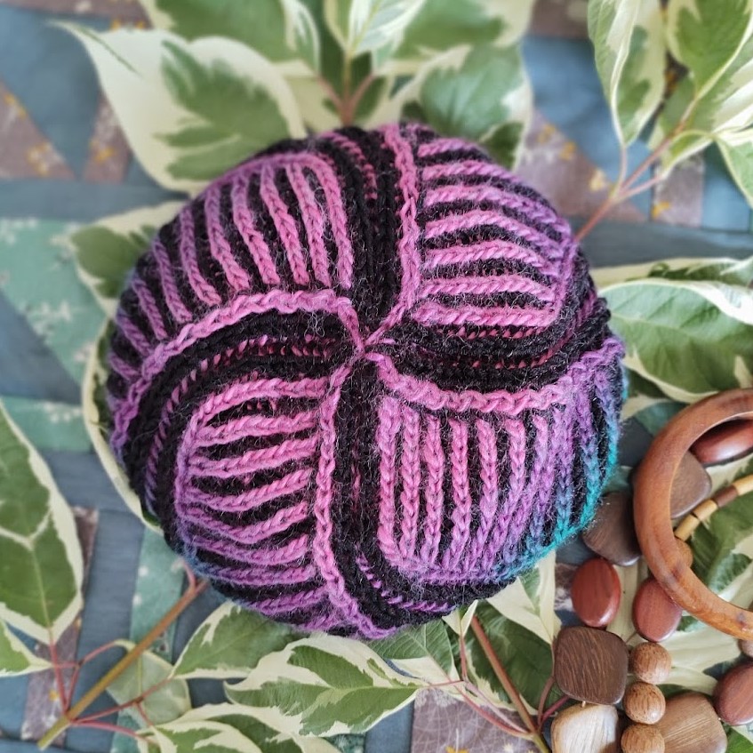 A crown of a brioche hat. Purple stripes join at the crown, separated by larger black stripes