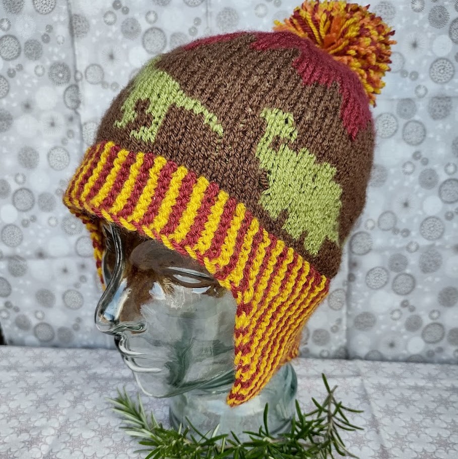 A hat bobble hat with ear flaps faces the camera at an angle. Part of a t-rex and ankylosaurus can be seen