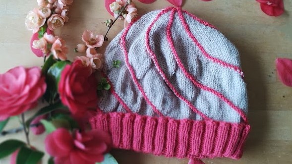 A cream hat with pink swirling lines lies on a table surrounded by flowers of a similar colour